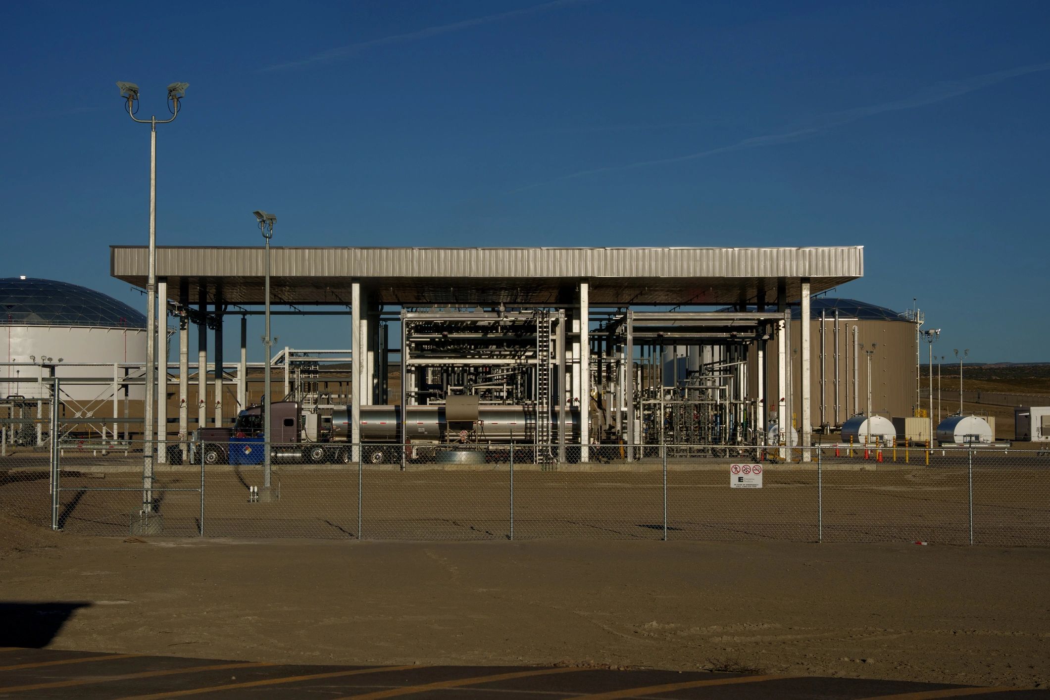 Tanker truck at fuel terminal loading rack behind perimeter fencing